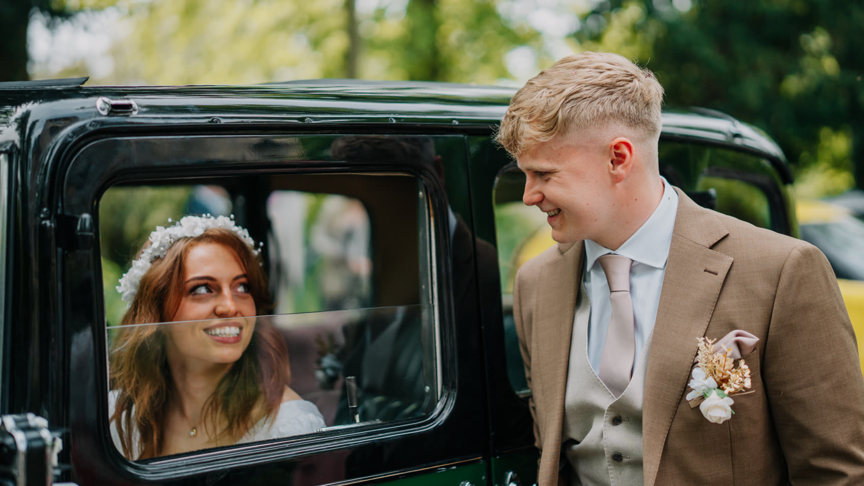 A bride in the window of a vintage car, the groom beside her